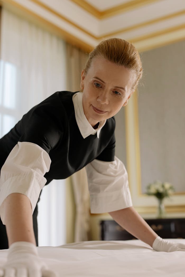 Crafting Captivating Headlines: Your awesome post title goes here A housekeeper in uniform skillfully arranges bed linen in a luxurious hotel room.
